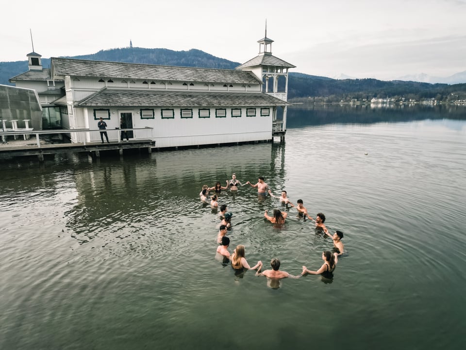 Gruppe steht Hand in Hand im Wörthersee vor dem historischen Badehaus
