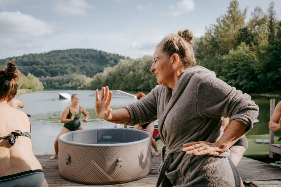 Teilnehmerin macht im Bademantel eine Aufwärmübung am See